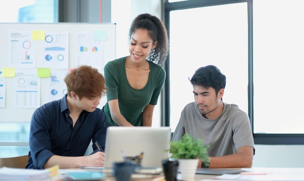 Gruppo di giovani uomini d'affari asiatici in abbigliamento casual intelligente che lavorano insieme nell'ufficio creativo utilizzando il laptop