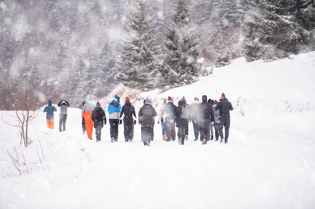 gruppo di giovani uomini d'affari che camminano attraverso il bellissimo paesaggio invernale con fiocchi di neve intorno a loro durante un team building nella foresta di montagna