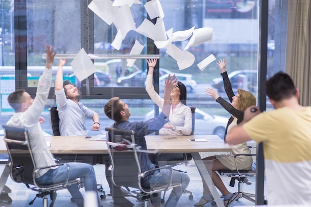 Gruppo di giovani uomini d'affari che lanciano documenti e sembrano felici mentre celebrano il successo nei loro posti di lavoro nell'ufficio di avvio