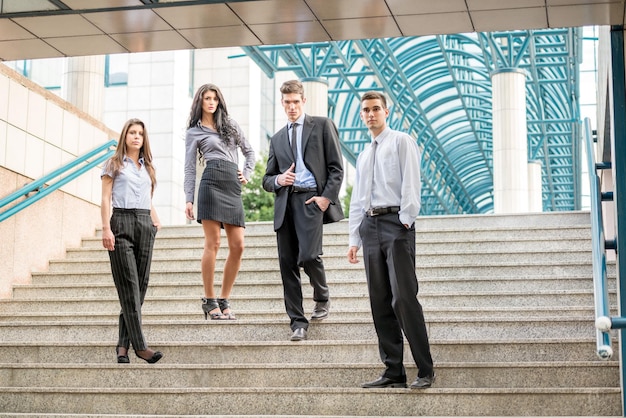 Gruppo di giovani uomini d'affari, elegantemente vestiti, in piedi sui gradini del palazzo dell'azienda.