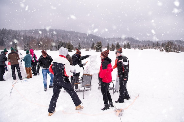 gruppo di giovani uomini d'affari felici che hanno una competizione nella creazione di pupazzi di neve mentre si godono una giornata invernale innevata con fiocchi di neve intorno a loro durante un team building nella foresta di montagna