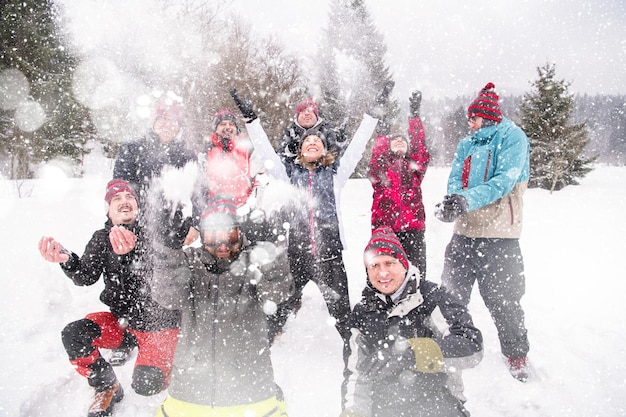 gruppo di giovani uomini d'affari felici che si divertono a lanciare neve in aria mentre si godono una giornata invernale innevata con fiocchi di neve intorno a loro durante un team building nella foresta di montagna