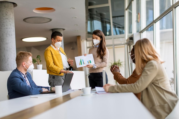 Gruppo di giovani uomini d'affari multietnici che lavorano insieme con maschere protettive per il viso e preparano un nuovo progetto per una riunione in ufficio