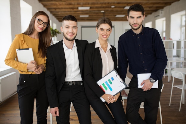 Gruppo di giovani uomini d'affari sorridenti in giacca e cravatta che guardano sognante a porte chiuse insieme mentre trascorrono del tempo al lavoro in un ufficio moderno