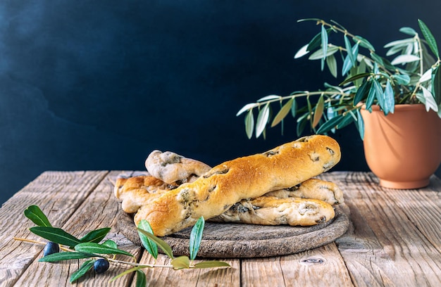 Gruppo di grissini ripieni di olive verdi tagliere ionico ramo di olivo olive in ciotola su tavolo di legno con sfondo scuro