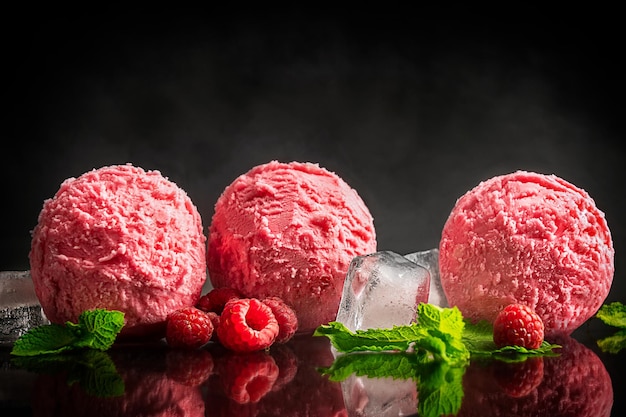 Gruppo di palline di gelato al lampone congelate che posano con cubetti di ghiaccio, foglie di menta e bacche sul nero