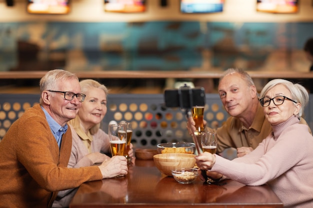 Gruppo di persone anziane moderne che scattano foto selfie mentre bevono birra al bowling e si godono la serata con gli amici, copia spazio