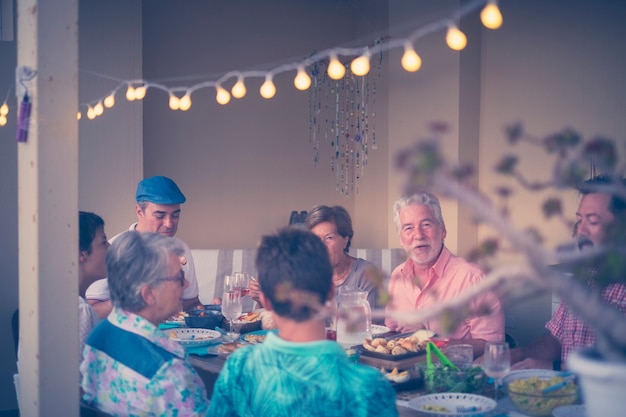 Gruppo di persone che cenano insieme a casa sulla terrazza all'aperto divertendosi e sorridendo