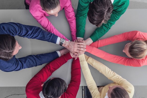 Gruppo di persone che si prendono per mano in pila seduti attorno al tavolo