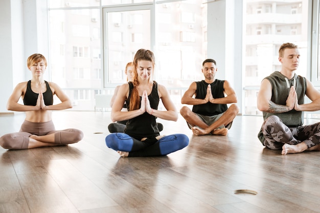 Gruppo di persone che si siedono e che meditano nello studio di yoga