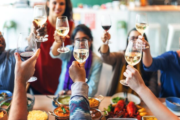 Gruppo di persone diverse che brindano con bicchieri di vino a un pasto festivo Gruppo diversificato che gode di cibo e bevande Celebrazione con amici diversi che condividono gioia e risate
