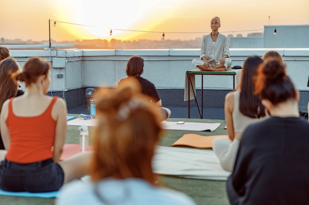 Gruppo di persone diverse stanno facendo pratiche di yoga meditativo sul tetto su un bel tramonto in una sera d'estate