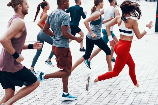 Gruppo di persone in abbigliamento sportivo che fanno jogging mentre si esercitano sul marciapiede all'aperto