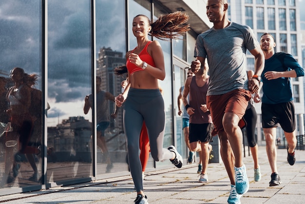 Gruppo di persone in abbigliamento sportivo che fanno jogging mentre si esercitano sul marciapiede all'aperto