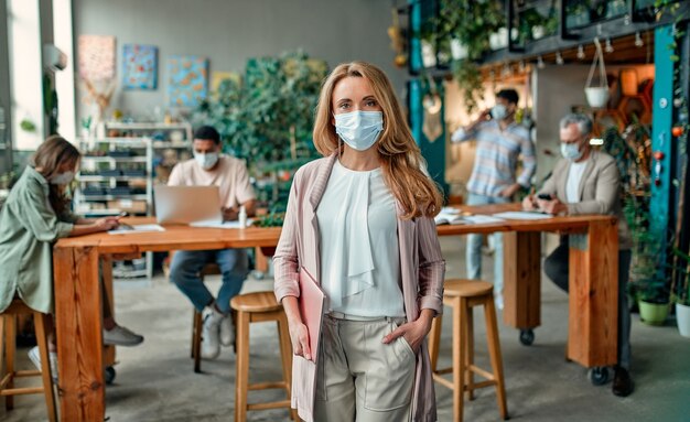 Gruppo di persone multirazziali che lavorano in un ufficio moderno durante il coronavirus. Giovani uomini d'affari e capo senior stanno lavorando insieme indossando maschere protettive per il viso. Misure preventive durante il Covid-19