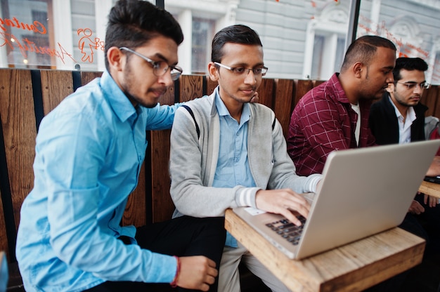 Gruppo di quattro studenti maschi adolescenti indiani. I compagni di classe trascorrono del tempo insieme e lavorano ai laptop.
