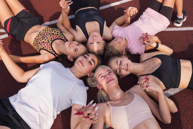 Gruppo di ragazze in forma stanche e felici che riposano sul pavimento allo stadio