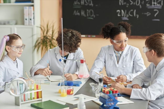 Gruppo di scolari che indossano camici da laboratorio durante la lezione di esperimenti scientifici