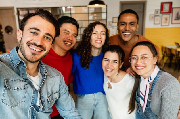 Gruppo di sei amici multirazziali che scattano una foto selfie con lo smartphone in un ristorante