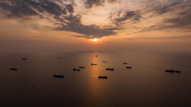 Gruppo di silhouette di nave portacontainer che galleggia in mare medio e sullo sfondo del tramonto