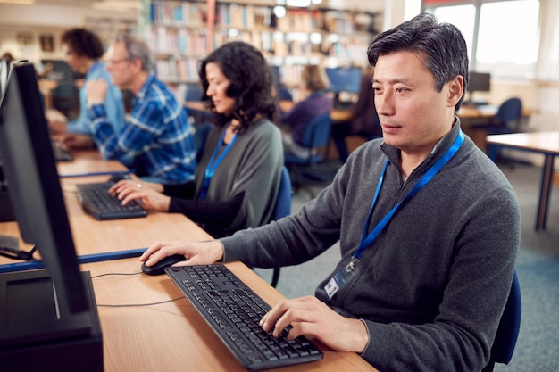 Gruppo di studenti adulti maturi in classe che lavorano al computer nella biblioteca del college