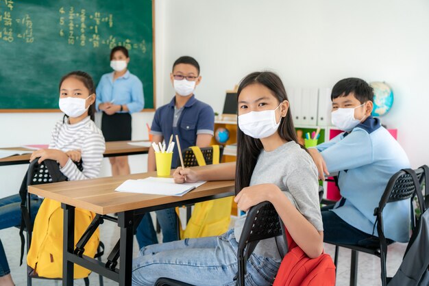 Gruppo di studenti asiatici della scuola elementare che indossano le maschere protettive