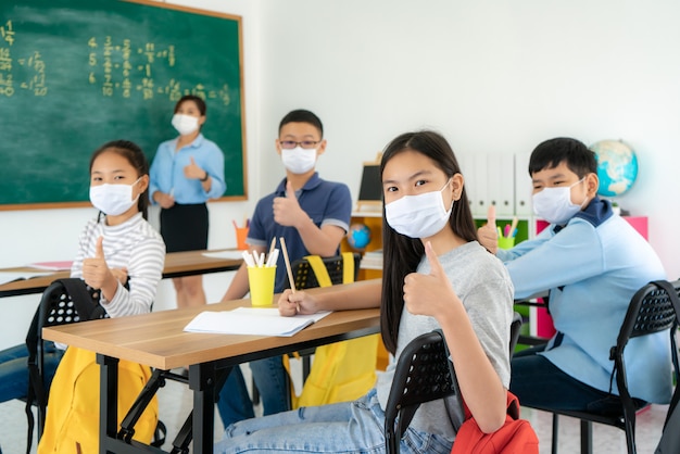 Gruppo di studenti asiatici della scuola elementare che indossano le maschere protettive