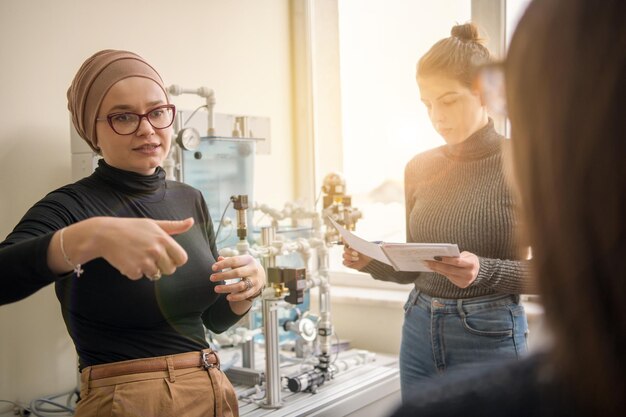 Gruppo di studenti che fanno pratica tecnica professionale con una giovane insegnante musulmana nell'aula elettronica, concetto di istruzione e tecnologia