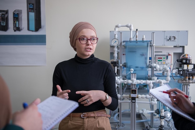 Gruppo di studenti che fanno pratica tecnica professionale con una giovane insegnante musulmana nell'aula elettronica, concetto di istruzione e tecnologia