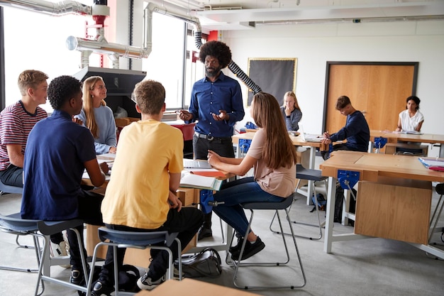 Gruppo di studenti delle scuole superiori seduti ai banchi di lavoro che ascoltano l'insegnante nella lezione di design e tecnologia