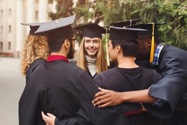 Gruppo di studenti multietnici che si abbracciano il giorno della laurea all'università, copia spazio. Istruzione, qualifica e concetto di abito.