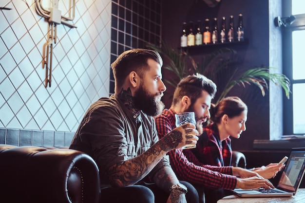 Gruppo di studenti seduti sul divano che riposano in un bar e lavorano con un laptop su un progetto comune.