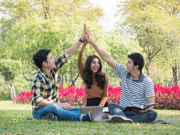 Gruppo di studenti universitari dando il cinque e divertirsi insieme mentre si fa i compiti al parco