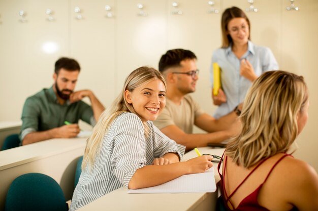 Gruppo di studenti universitari in aula con giovane assistente docente femminile