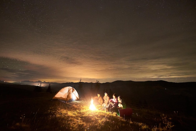 Gruppo di turisti con la chitarra bruciando falò sotto il cielo stellato scuro con la costellazione della Via Lattea.