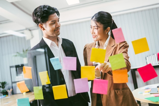 Gruppo di uomini d'affari asiatici di successo lavoro di squadra Brainstorming meeting con appunti adesivi sulla parete di vetro per nuove idee Utilizzando la metodologia agile per il business in un ufficio di startup tecnologico