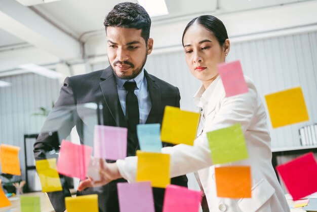 Gruppo di uomini d'affari asiatici di successo lavoro di squadra Brainstorming meeting con appunti adesivi sulla parete di vetro per nuove idee Utilizzando la metodologia agile per il business in un ufficio di startup tecnologico