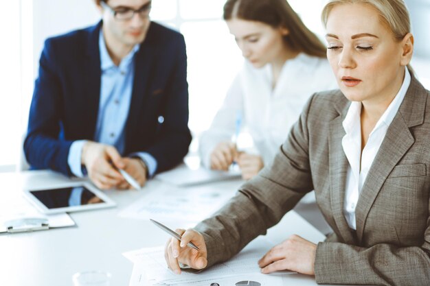 Gruppo di uomini d'affari che discutono di domande durante la riunione in un ufficio moderno. Colpo in testa della donna d'affari alla trattativa. Concetto di lavoro di squadra, partnership e business.