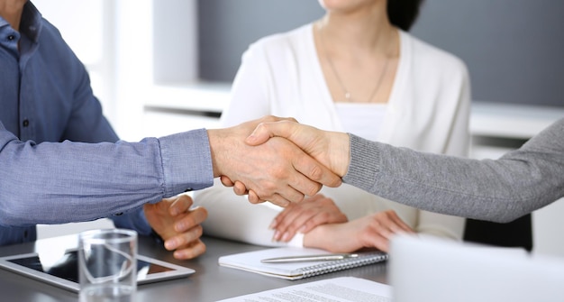 Gruppo di uomini d'affari che si stringono la mano dopo aver discusso di domande e raggiunto un accordo durante la riunione in un ufficio moderno. Primo piano della stretta di mano. Concetto di lavoro di squadra, partnership e business.