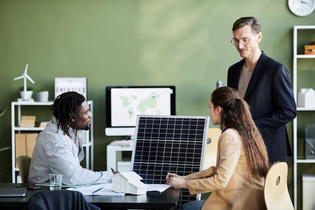 Gruppo di uomini d'affari che sviluppano pannelli solari per l'energia alternativa mentre sono seduti al tavolo a