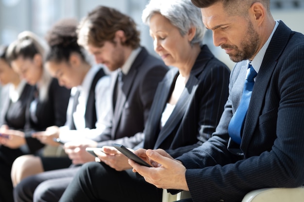 Gruppo di uomini d'affari con smartphone seduti in fila.