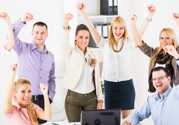 Gruppo di uomini d'affari di successo felici in ufficio, con le braccia alzate che guarda l'obbiettivo.