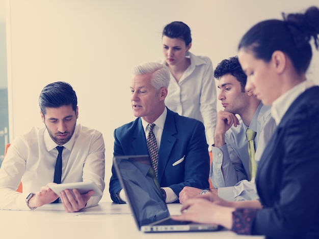 gruppo di uomini d'affari in riunione al moderno ufficio di avvio, uomo anziano come leader che guarda su tablet e laptop presentazione della sua squadra