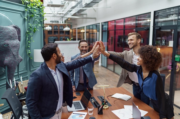 Gruppo di uomini d'affari multietnici che uniscono le mani stando in piedi nel moderno coworking