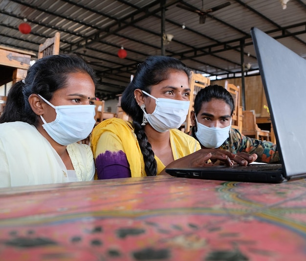 Gruppo di uomini e donne indiani che indossano una maschera mentre guardano un computer portatile