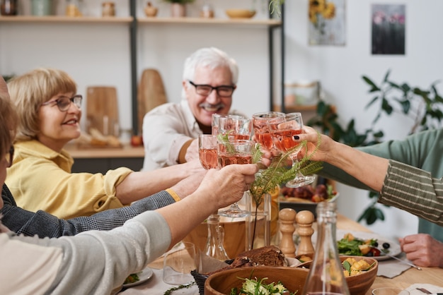 Gruppo di vecchi amici che brindano con bicchieri di vino rosso seduti al tavolo da pranzo