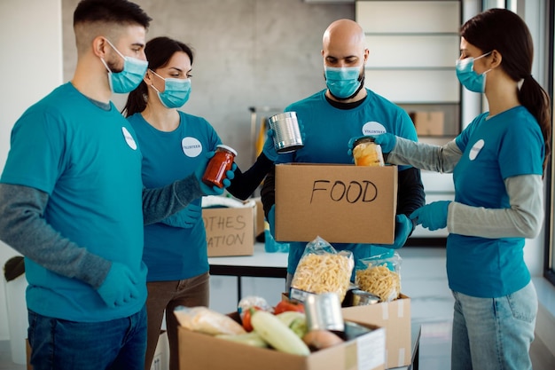 Gruppo di volontari con maschere facciali che collaborano mentre imballano il cibo donato in scatole di cartone