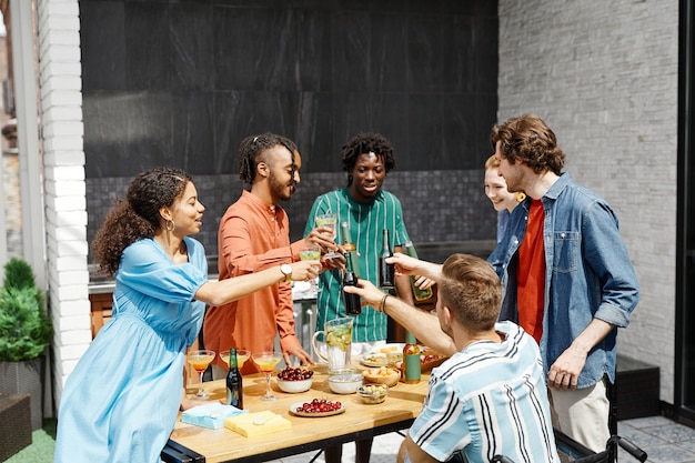 Gruppo eterogeneo di amici che si godono la cena sulla terrazza all'aperto alla luce del sole e bicchieri tintinnanti i