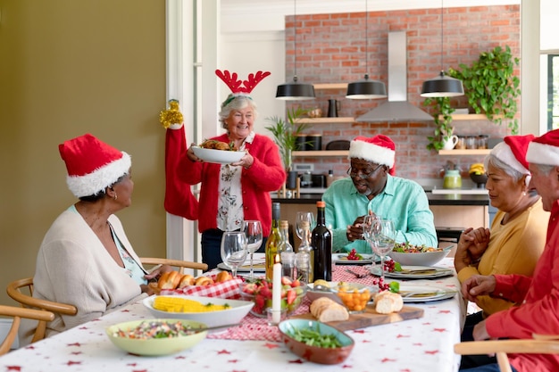 Gruppo eterogeneo di amici senior felici in cappelli da vacanza che celebrano il Natale insieme a casa