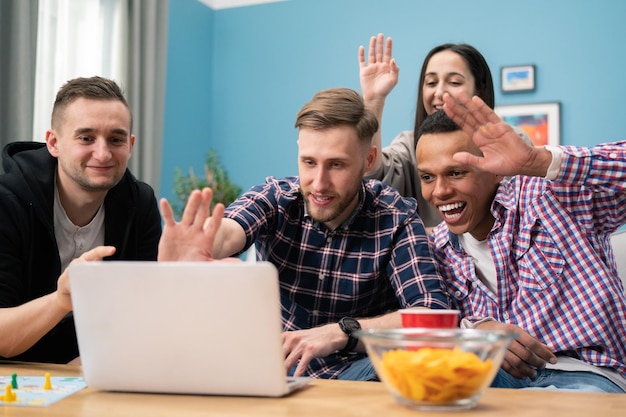 Gruppo eterogeneo di amici usa il laptop nel soggiorno in diretta streaming di giovani studenti sorridenti